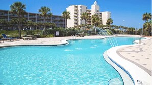 A swimming pool with a curved design, surrounded by palm trees and a building with multiple balconies. - 10th Floor Sweeping Views of the Gulf. Steps from Beach Access. (Pensacola Beach)