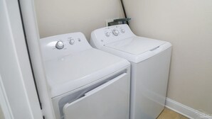 A laundry room with two white front-loading washing machines and a mop leaning against the wall. - 10th Floor Sweeping Views of the Gulf. Steps from Beach Access. (Pensacola Beach)