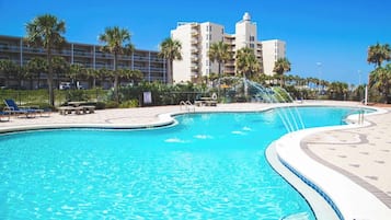 Una piscina dalla forma sinuosa, circondata da palme e un edificio con numerosi balconi.