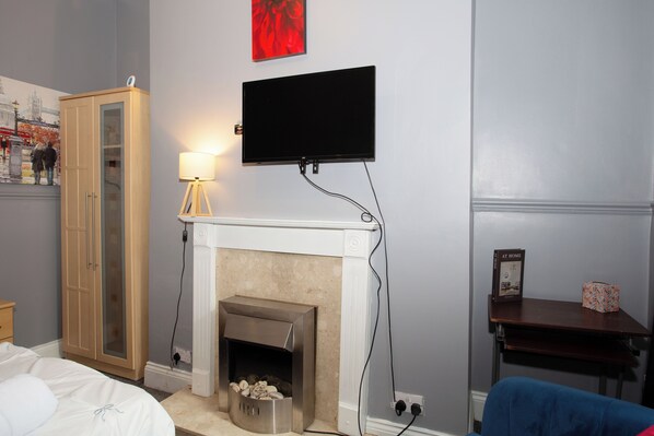 A room with a fireplace, a television mounted on the wall, a lamp, and a bed. - The Vacationers (Sunderland)