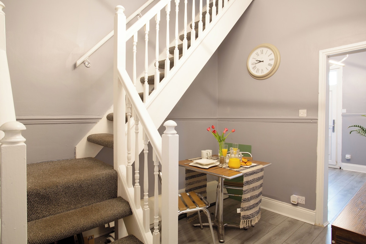 A staircase with a white railing, a dining table with breakfast items, and a wall clock.