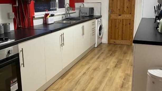 A kitchen with white cabinets, a wooden floor, a microwave, and a washing machine.