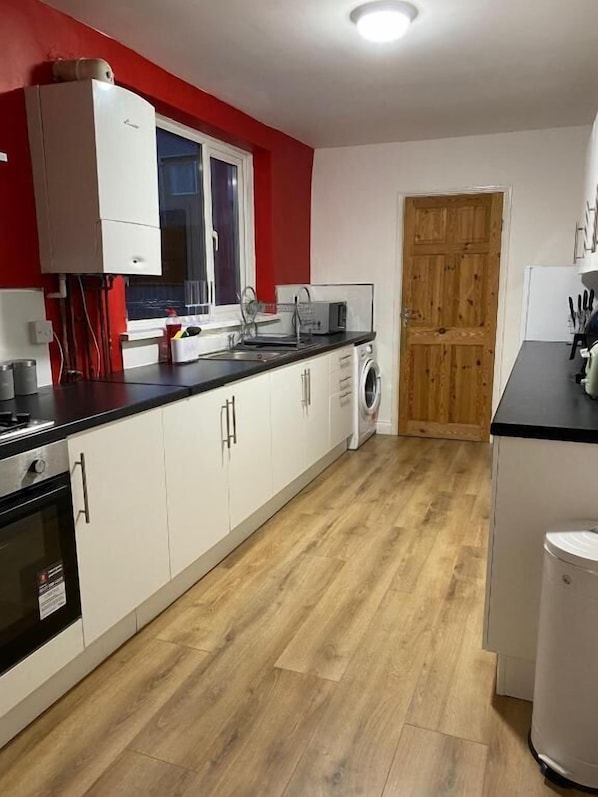 A kitchen with white cabinets, a wooden floor, a microwave, and a washing machine.