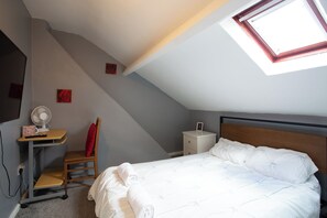 A bedroom with a sloped ceiling, a bed, a desk with a chair, a nightstand, and a wall-mounted fan. - The Vacationers (Sunderland)