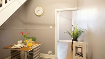 Una habitación con una mesa de comedor dispuesta para el desayuno, un reloj en la pared y una planta cerca de la puerta.