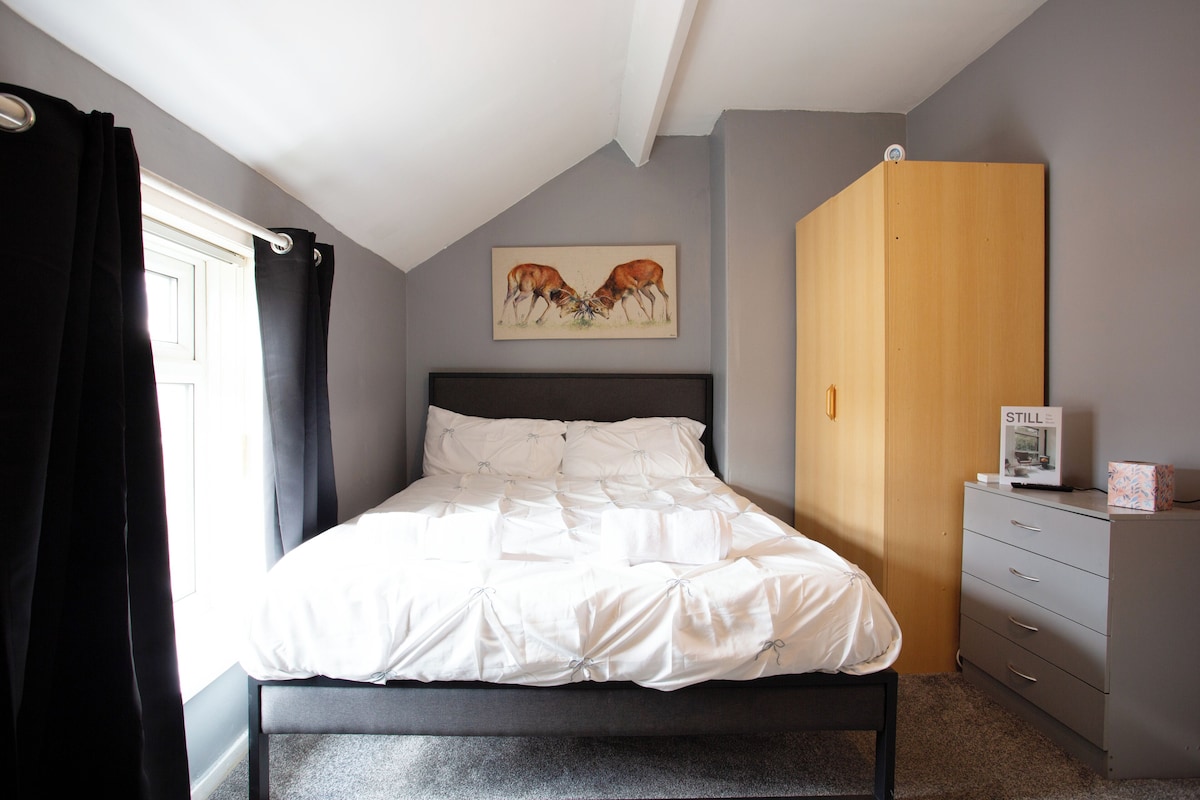 A bedroom with a bed, a wardrobe, a painting, and a window with curtains.