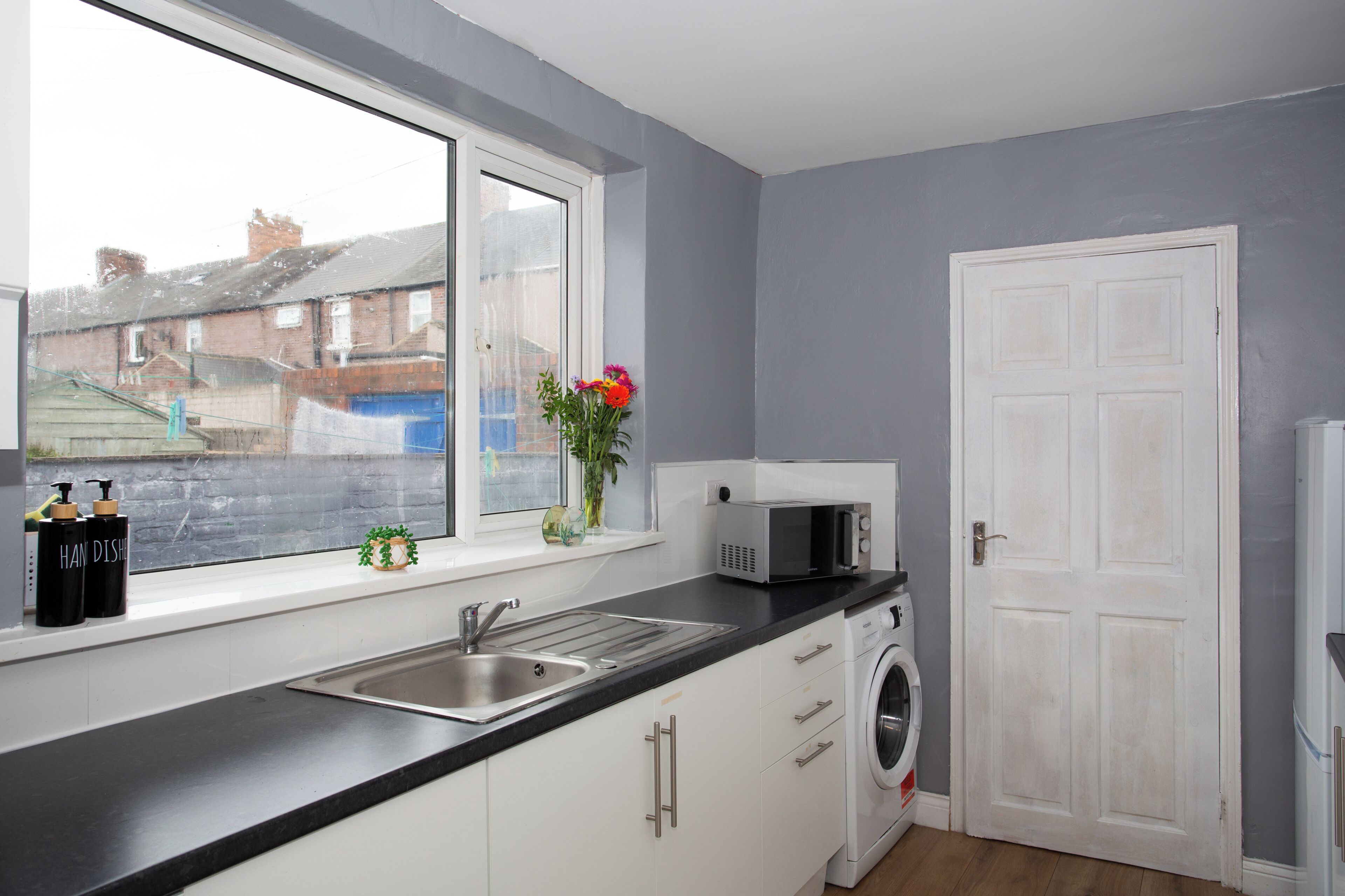 A kitchen with a window, a sink, a microwave, and a washing machine.
