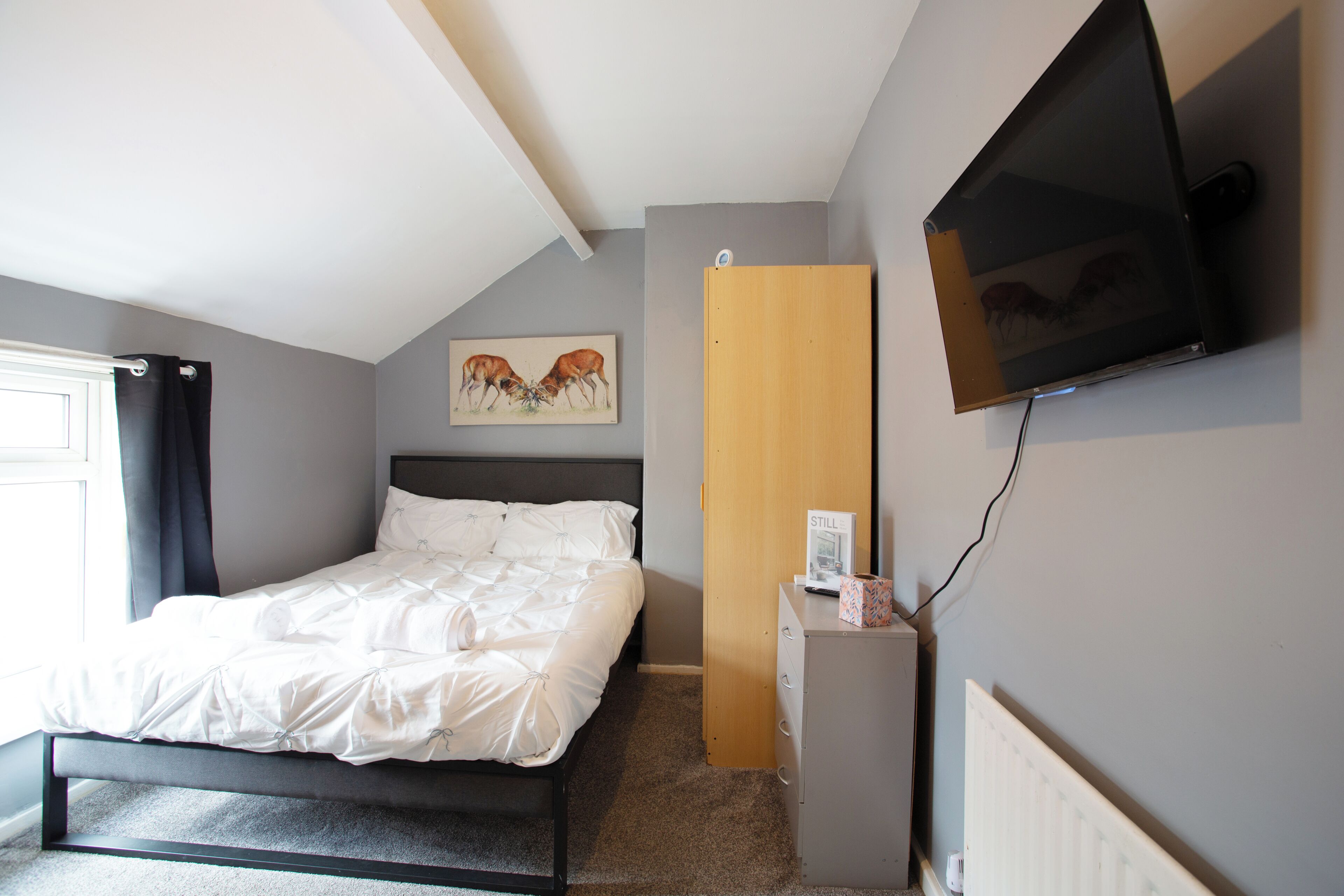 A bedroom with a bed, a television mounted on the wall, and a painting above the bed.