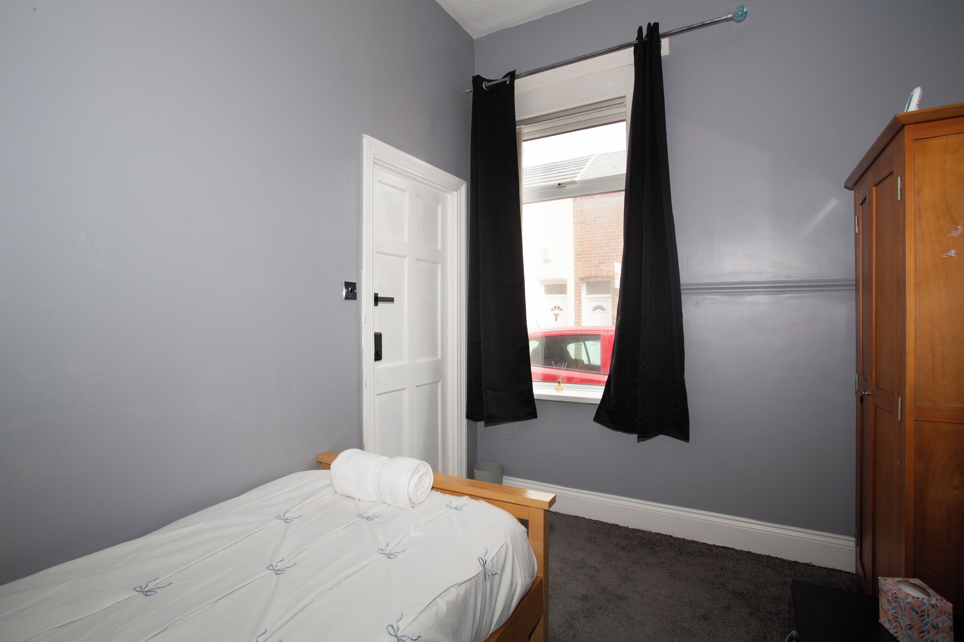 A bedroom with a single bed, a wardrobe, and a window with curtains.