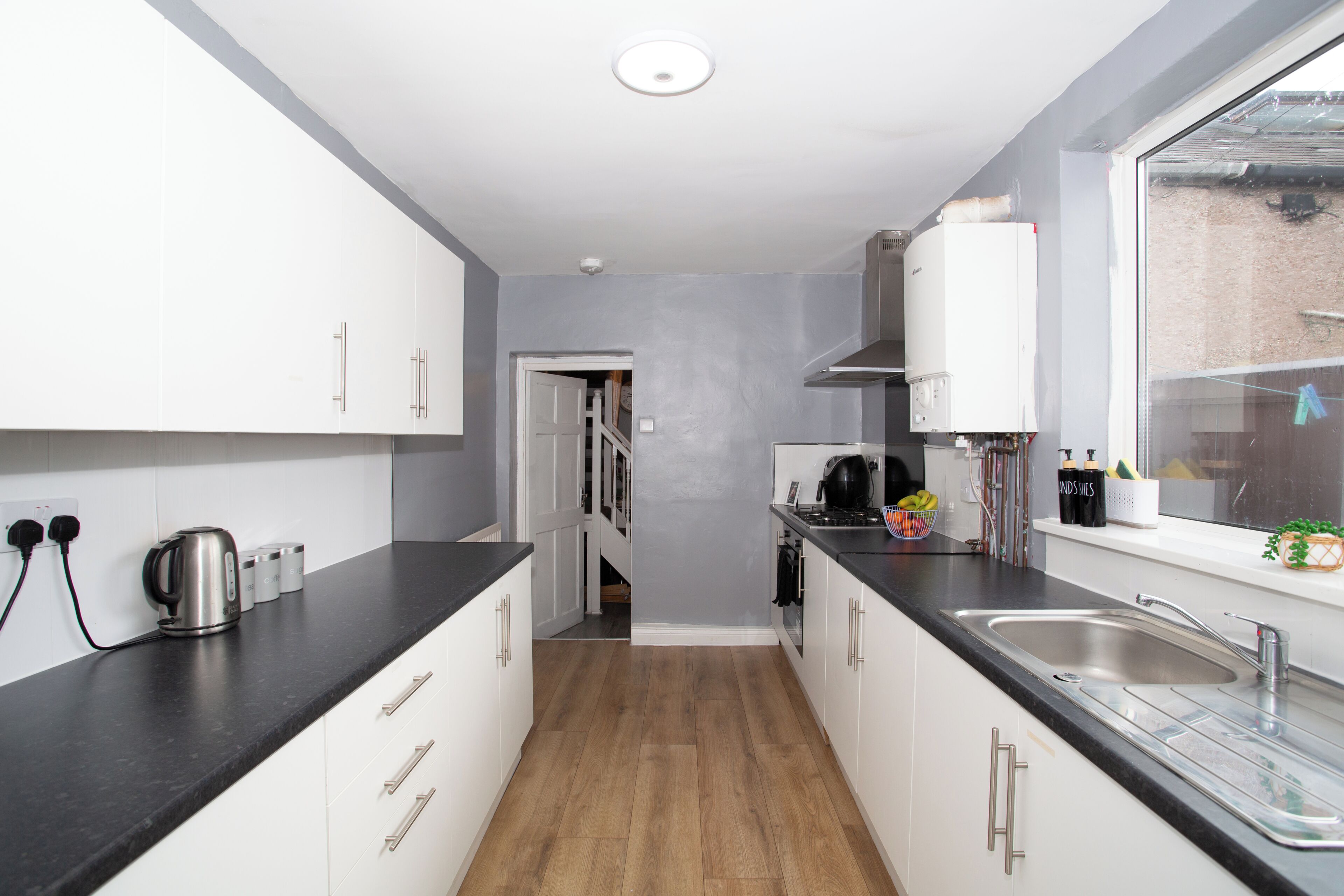 A modern kitchen with white cabinets, a black countertop, and a stainless steel kettle.