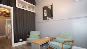 A room with two light green upholstered chairs, a wooden coffee table, and a dark wall with a vertical panel design.