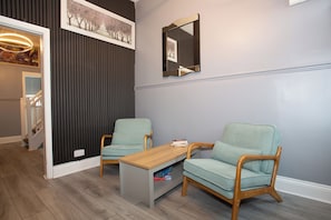 A room with two light green upholstered chairs, a wooden coffee table, and a dark wall with a vertical panel design.