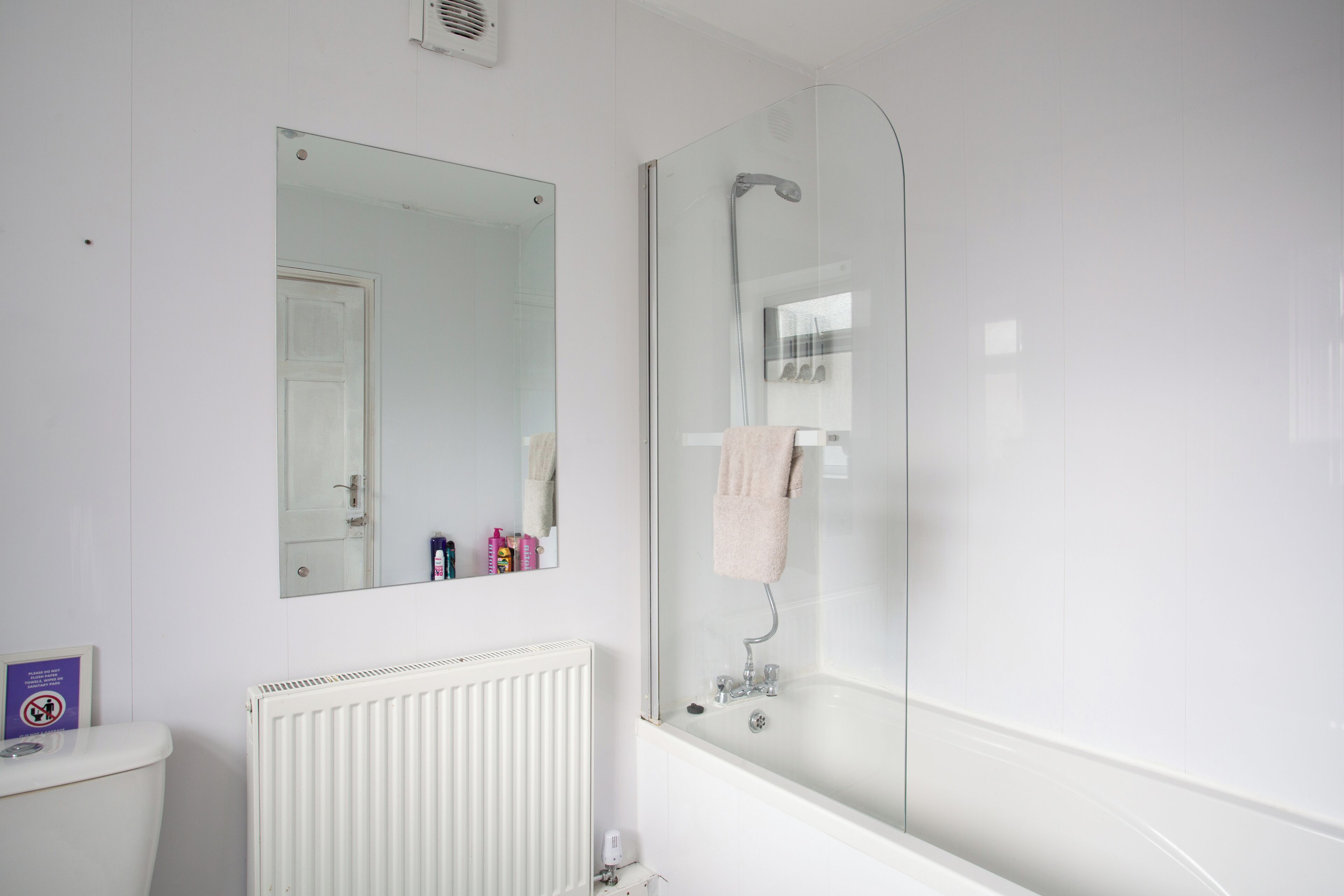 A bathroom with a white radiator, a mirror, and a glass-enclosed shower.