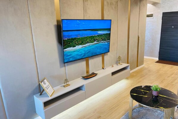 A modern hotel reception area with a flat-screen TV mounted on a wall, a reception desk, and a small round table with a plant.