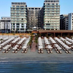 A beachfront hotel with multiple floors, outdoor seating areas with umbrellas, and a clear view of the ocean.