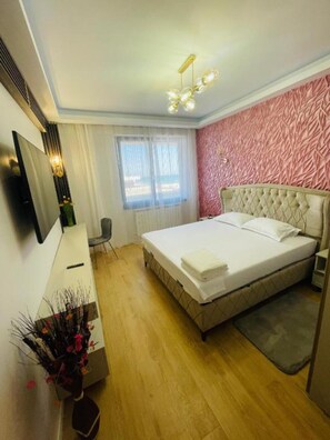 A bedroom with a bed, a desk, a chair, a TV, and a window.