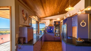 Een moderne keuken met uitzicht op het strand, een houten plafond en paarse kastjes.