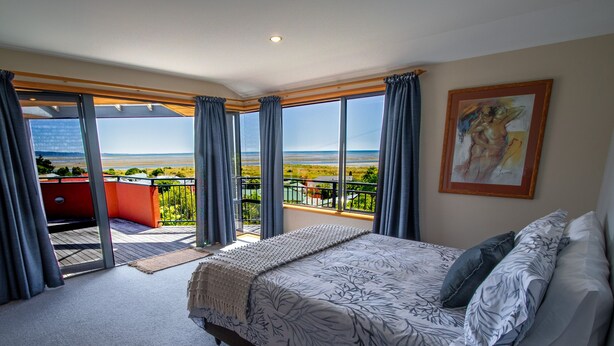 Een slaapkamer met een groot bed, uitzicht op zee en een balkon met een rode stoel.