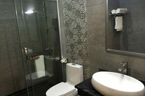 A bathroom with a glass shower enclosure, a toilet, a sink, and patterned tiles.
