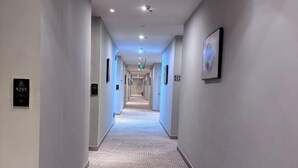 A hotel hallway with a patterned carpet, wall-mounted light switches, and a framed picture. - Fuxin Inn (Zhuhai Baitengtou ) (Zhuhai)