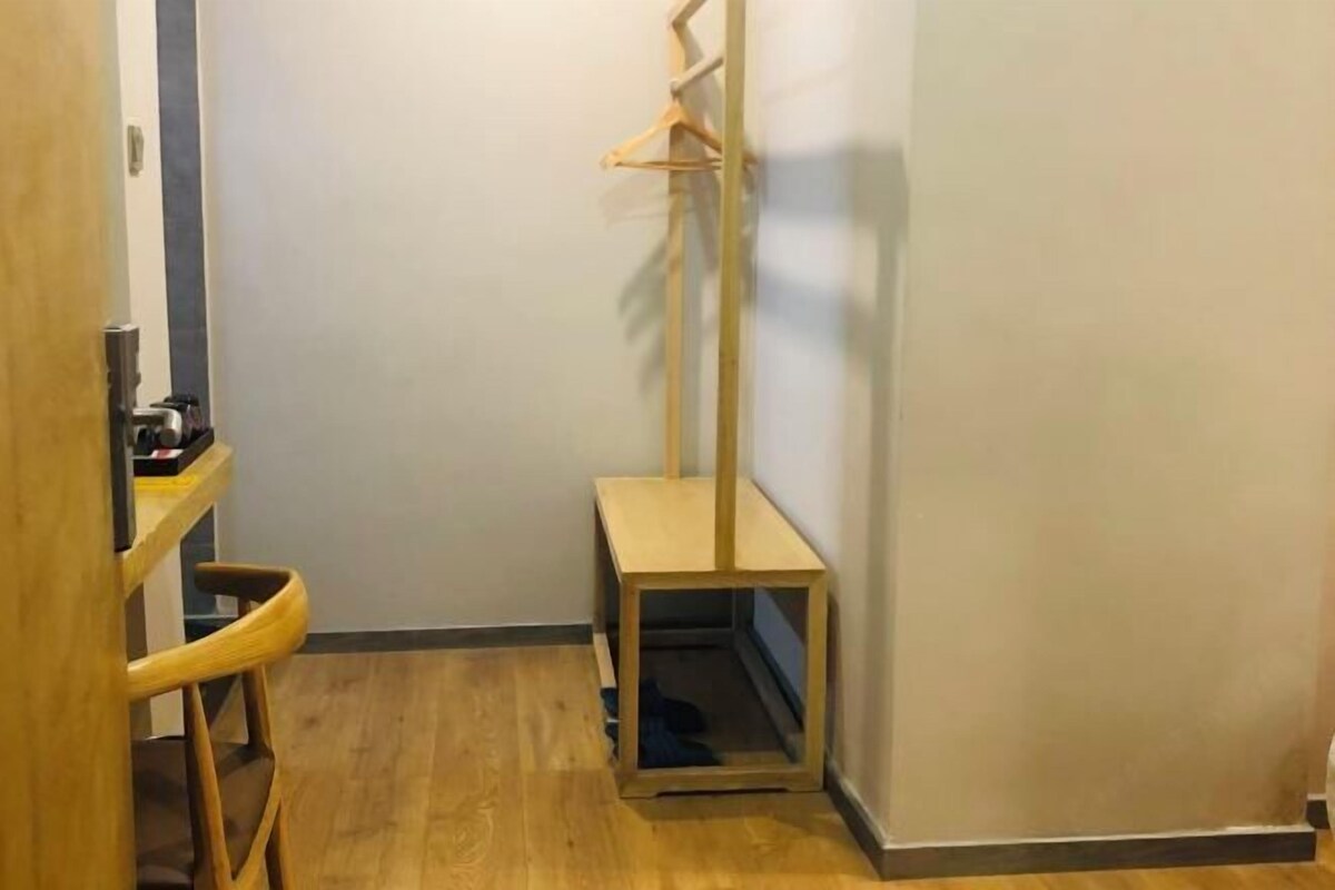 A corner room with a wooden floor, a small table, a chair, and a coat rack.