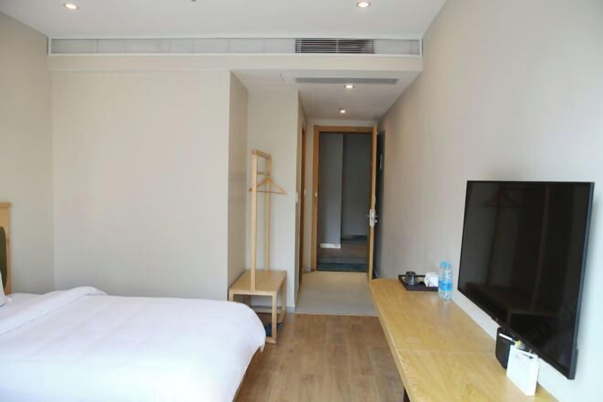 A hotel room with a bed, a TV, a wooden desk, and a wardrobe.