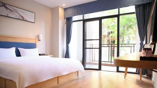 A hotel room with a large bed, a wooden headboard, a dining table, and a view through a glass door to the outside. - Fuxin Inn (Zhuhai Baitengtou ) (Zhuhai)