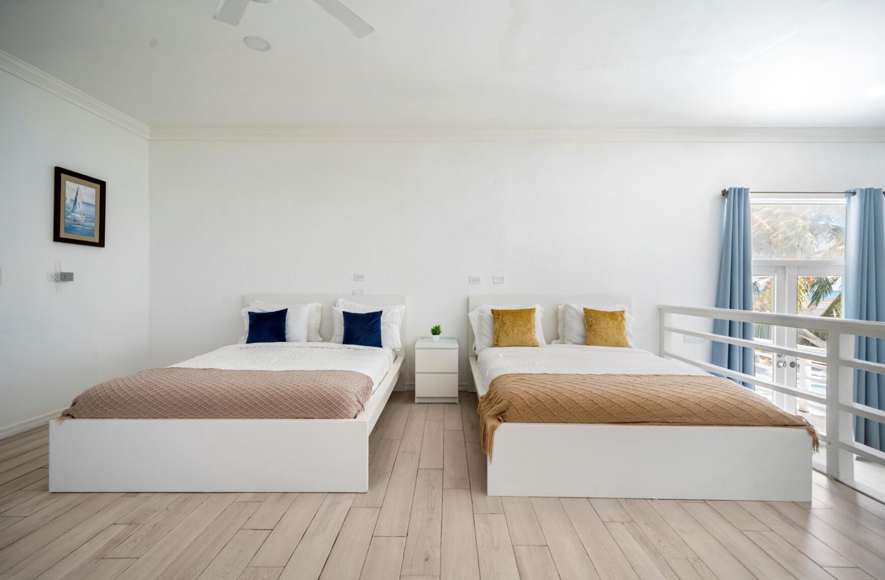 Une chambre d’hôtel avec deux lits, une petite table de chevet avec une lampe, une fenêtre avec des rideaux et un tableau encadré au mur.