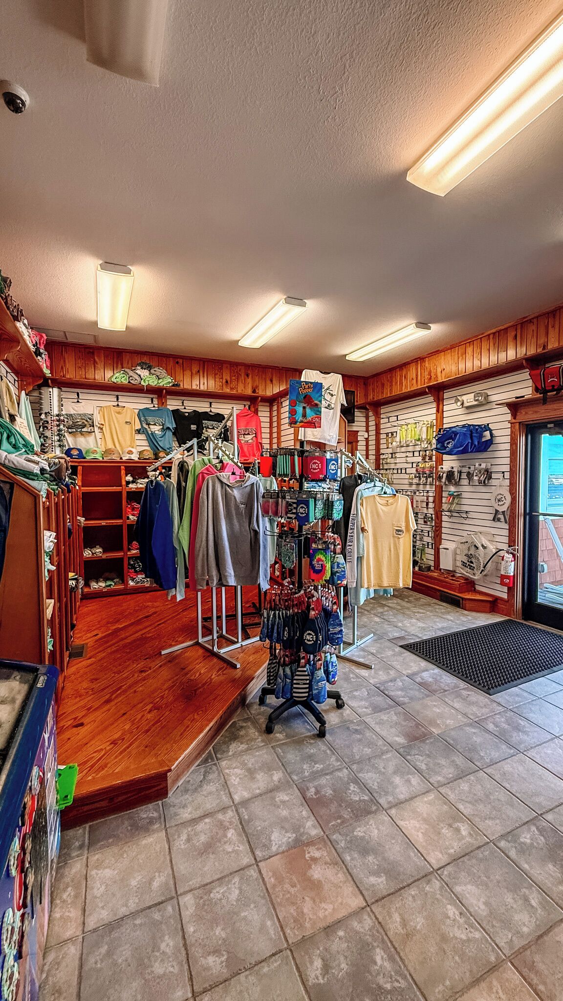 A retail store with wooden paneling, a variety of clothing and accessories on display, and a tiled floor.