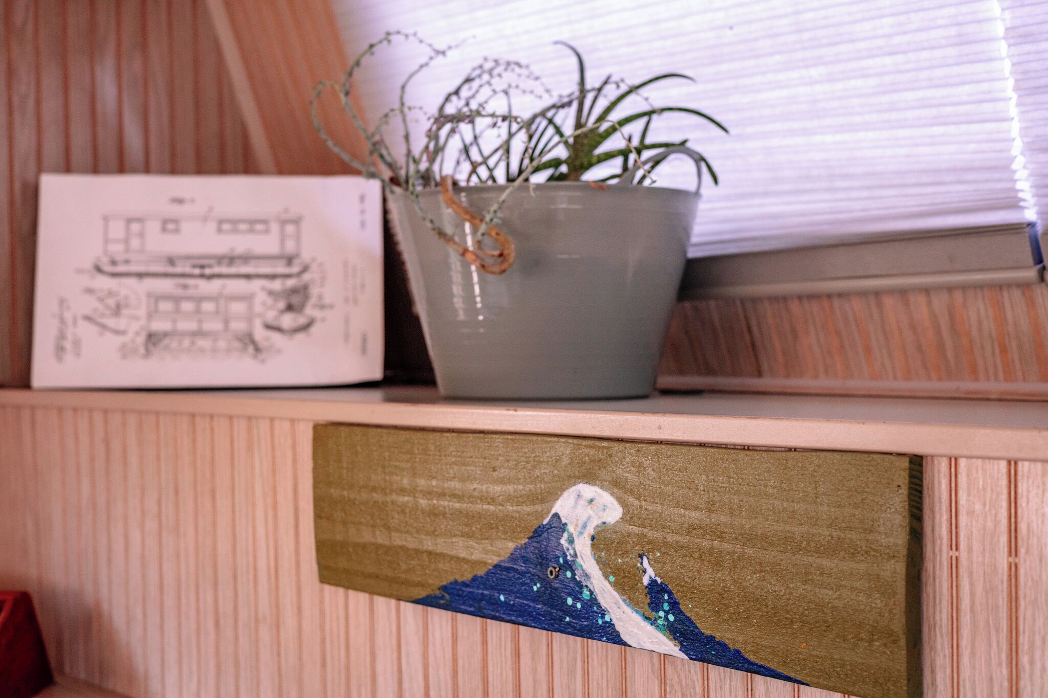 A shelf with a potted plant, a framed architectural drawing, and a framed artwork.