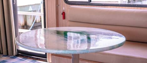 Una mesa redonda de vidrio con base metálica, ubicada frente a un banco con cojín color beige.