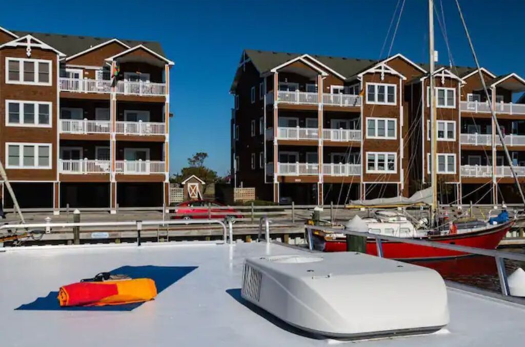 A marina with boats docked, a lifebuoy on the deck, and a building with balconies.