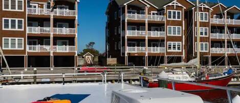 A marina with boats docked, a lifebuoy on the deck, and a building with balconies.