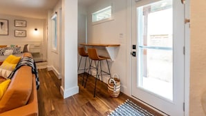 A modern living room with a sofa, a small dining area with chairs, and a door leading outside. - The Recovery Room-0.5 Mi to Beach & 0.3 to Sound (Kill Devil Hills)
