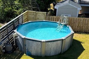 An above-ground swimming pool with a ladder, surrounded by a wooden fence and a grassy yard. - Knot On Call: OceanViews/Pool/MultiUsePath (Kill Devil Hills)