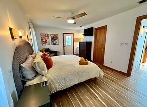 A bedroom with a bed, a ceiling fan, a TV, and a wooden floor. - Knot On Call: OceanViews/Pool/MultiUsePath (Kill Devil Hills)