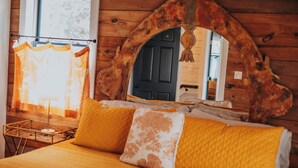 Ein Bett mit gelber Bettwäsche, einem Holzkopfschild und einem Spiegel mit rustikalem Design.