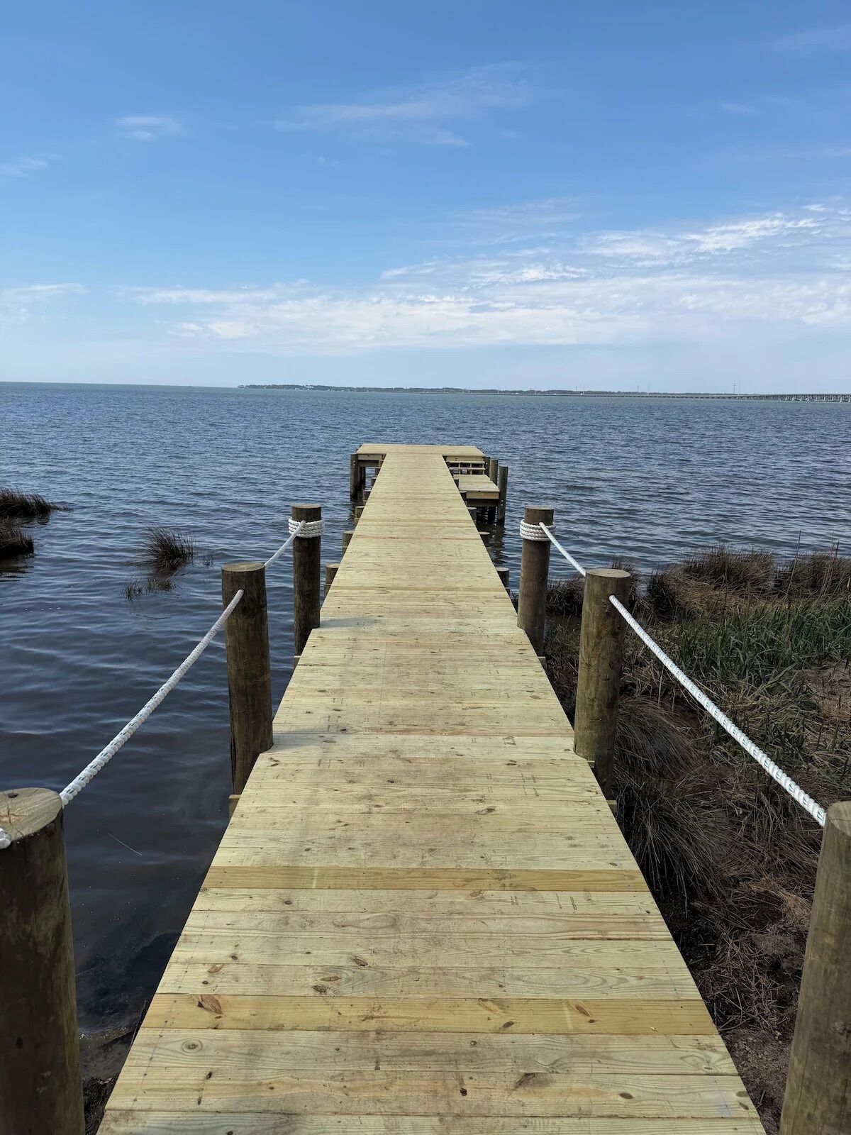 Une jetée en bois s’étendant dans une étendue d’eau calme, entourée de zones verdoyantes.