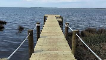 Une jetée en bois s’étendant dans une étendue d’eau calme, entourée de zones verdoyantes.