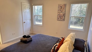 Une chambre avec un grand lit, deux fenêtres, une porte et des œuvres d’art accrochées au mur.