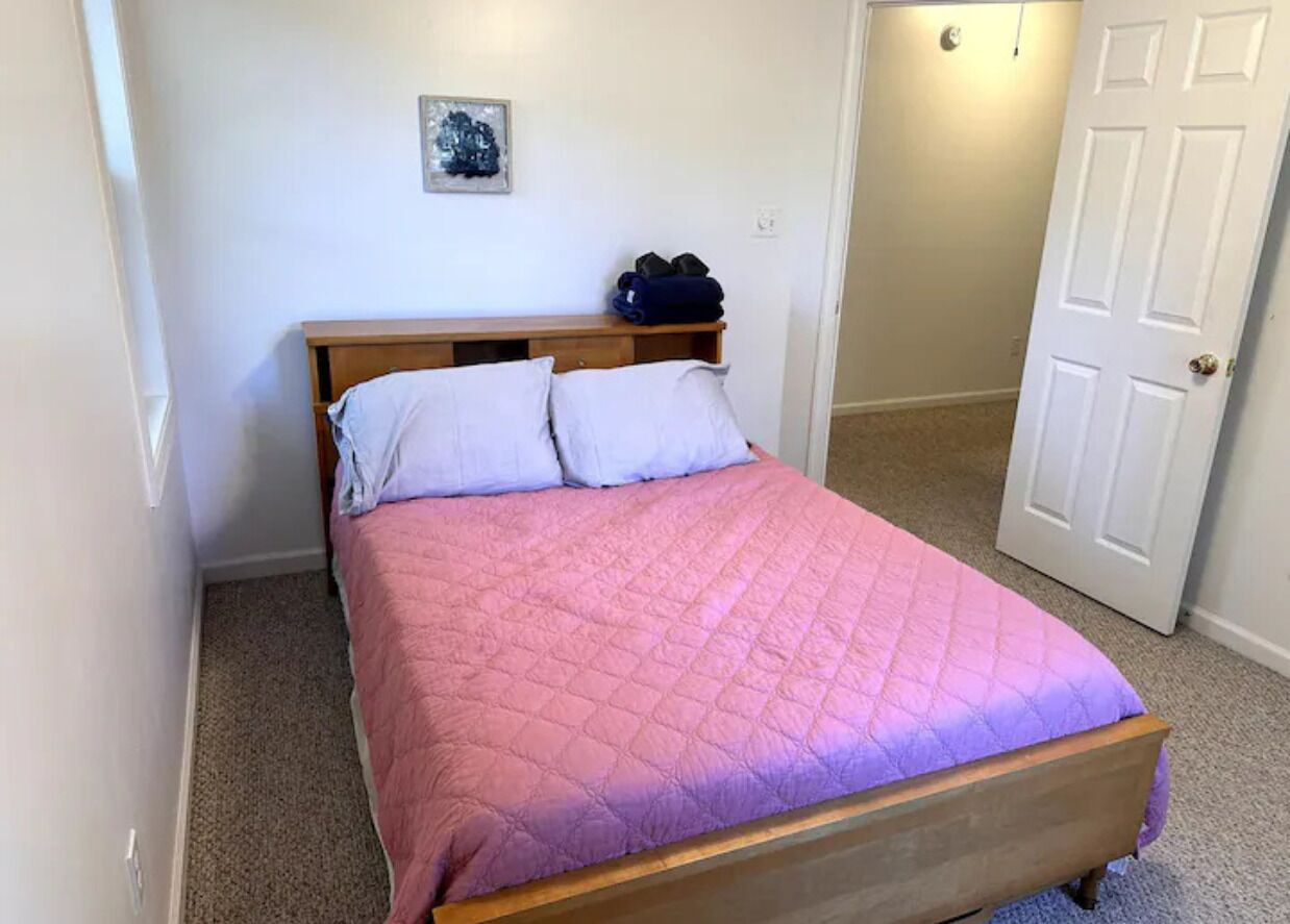 A single bed with a wooden frame and a pink quilted bedspread.