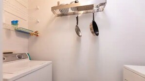 Un espace buanderie comprenant un lave-linge, un étendoir et un porte-casseroles suspendu.