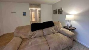 Un salon avec un canapé beige, un plaid noir, une lampe et une petite table.