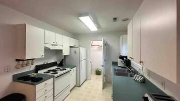 Una cocina compacta con armarios blancos, estufa, refrigerador y tostadora.