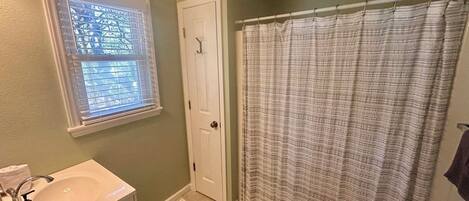 Une salle de bain comprenant des toilettes, un lavabo, une fenêtre avec stores, un rideau de douche et un tapis.