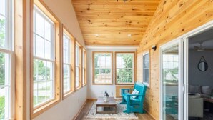 A spacious room with large windows, wooden ceiling, and a sliding glass door leading to an outdoor area.