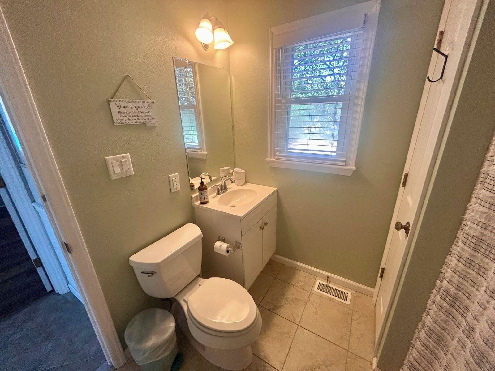 A bathroom with a toilet, sink, mirror, and window.