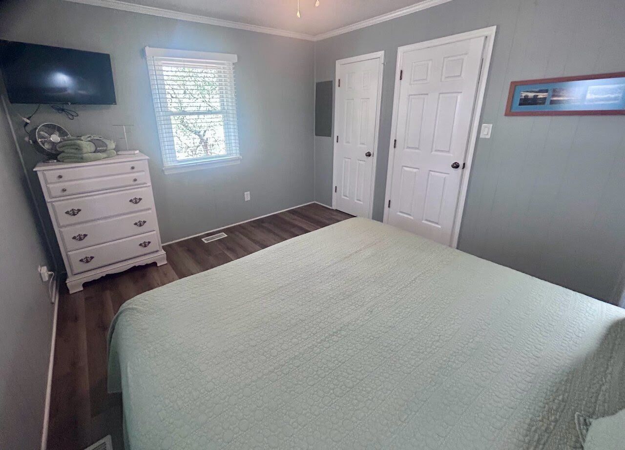 Een slaapkamer met een bed, een dressoir, een televisie en twee deuren.