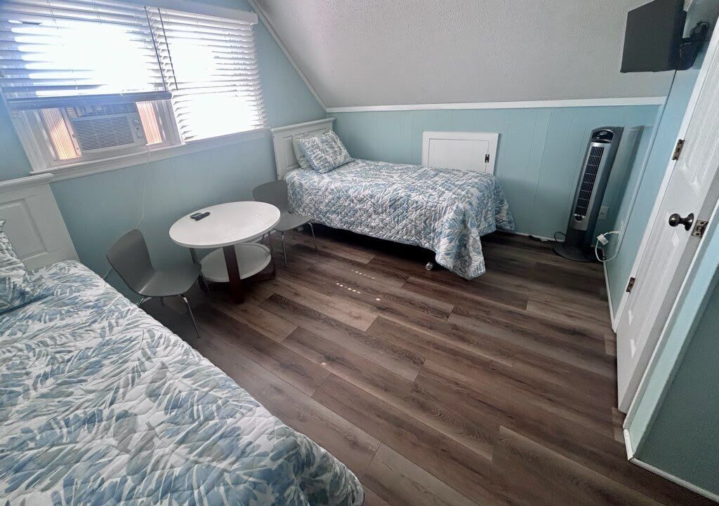 Una habitación con cama, una mesa redonda, dos sillas, un radiador y una puerta.