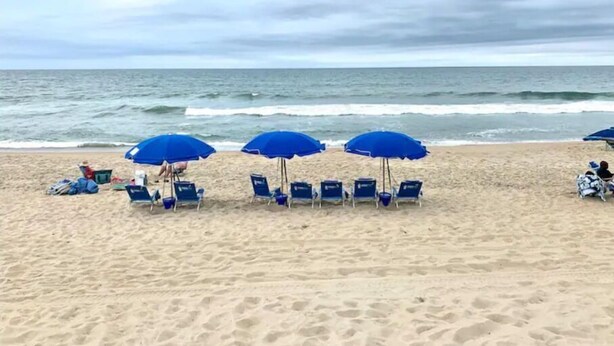 A beach with rows of blue umbrellas and chairs facing the ocean.